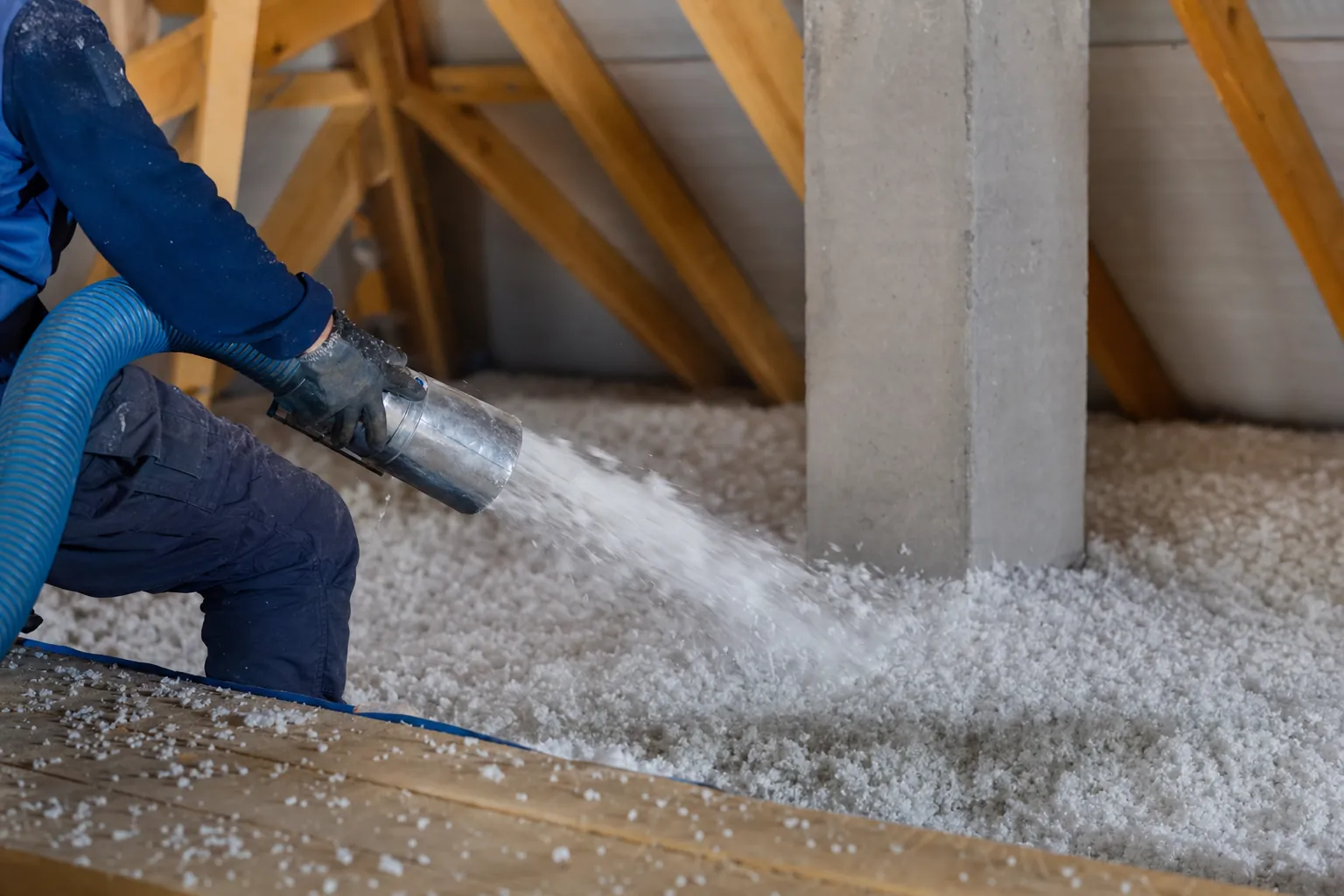 buse d'une machine à souffler projetant des flocons de laine minérale sur le plancher de combles perdus, formant une couche
